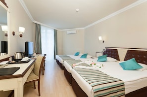 A hotel room with a desk, two beds, a television, and an air conditioning unit. - Nova Park (Manavgat)