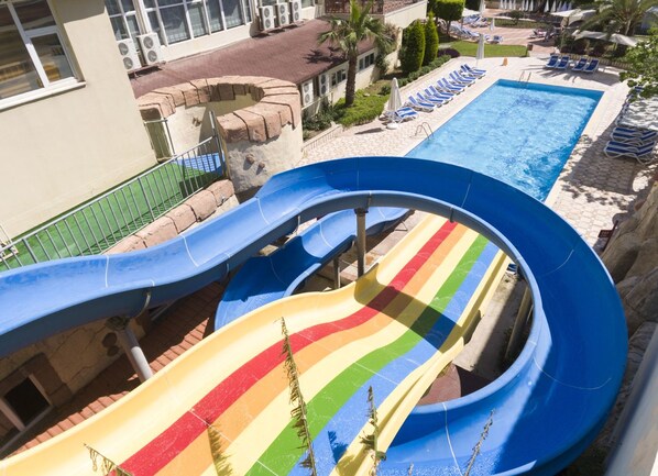 Um tobogã com design de arco-íris, uma piscina e cadeiras de descanso.