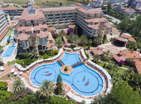 A hotel with multiple swimming pools, palm trees, and a central fountain. - Nova Park (Manavgat)