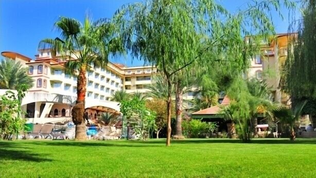 A hotel with a large courtyard, palm trees, and a building with multiple balconies. - Nova Park (Manavgat)