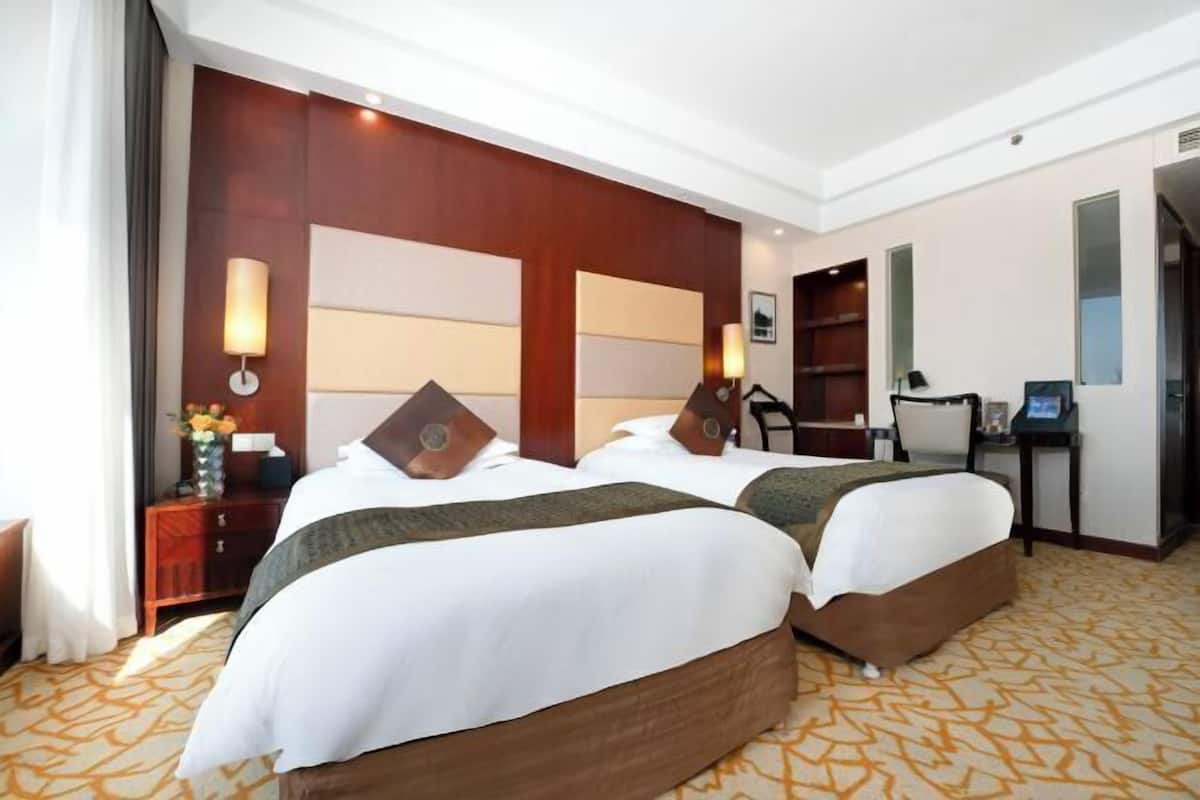 Una habitación de hotel con dos camas, un escritorio, una silla, una lámpara y una estantería.