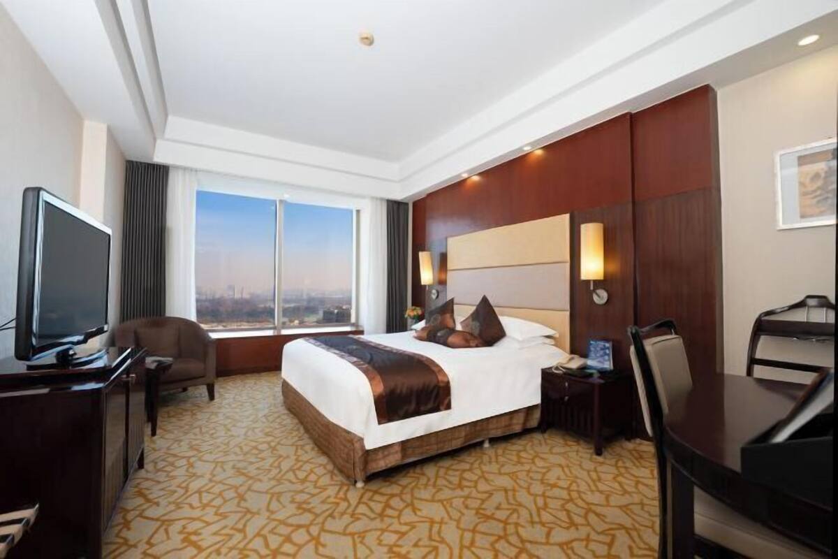 Habitación de hotel con una cama grande, un escritorio, una silla, un televisor y vistas de la ciudad.
