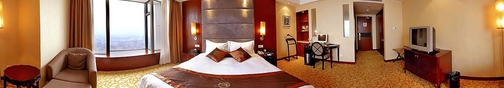 A hotel room with a large bed, a desk with a chair, a television, and a view of the city.