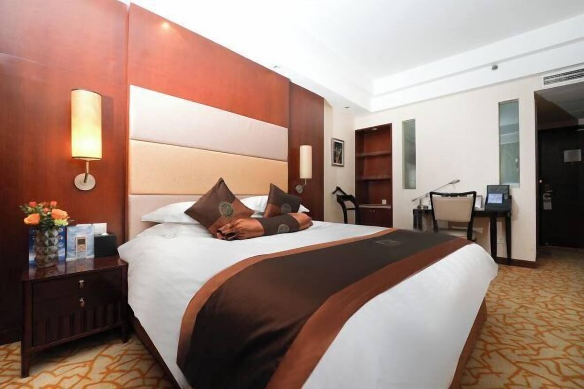 Habitación de hotel con una cama grande, una mesita de noche con lámpara, un escritorio con silla y una estantería.