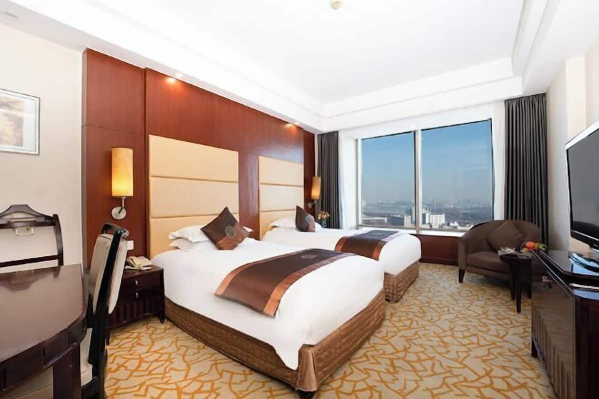 Habitación de hotel con dos camas, un escritorio, una silla, un televisor y un ventanal con vista a la ciudad.