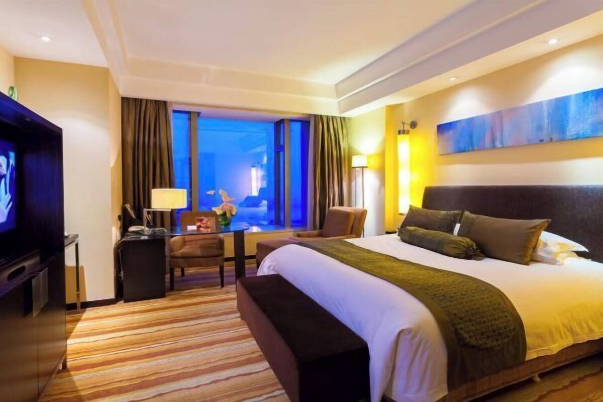 Habitación de hotel con una cama grande, televisión, escritorio con lámpara y vistas a la ciudad.