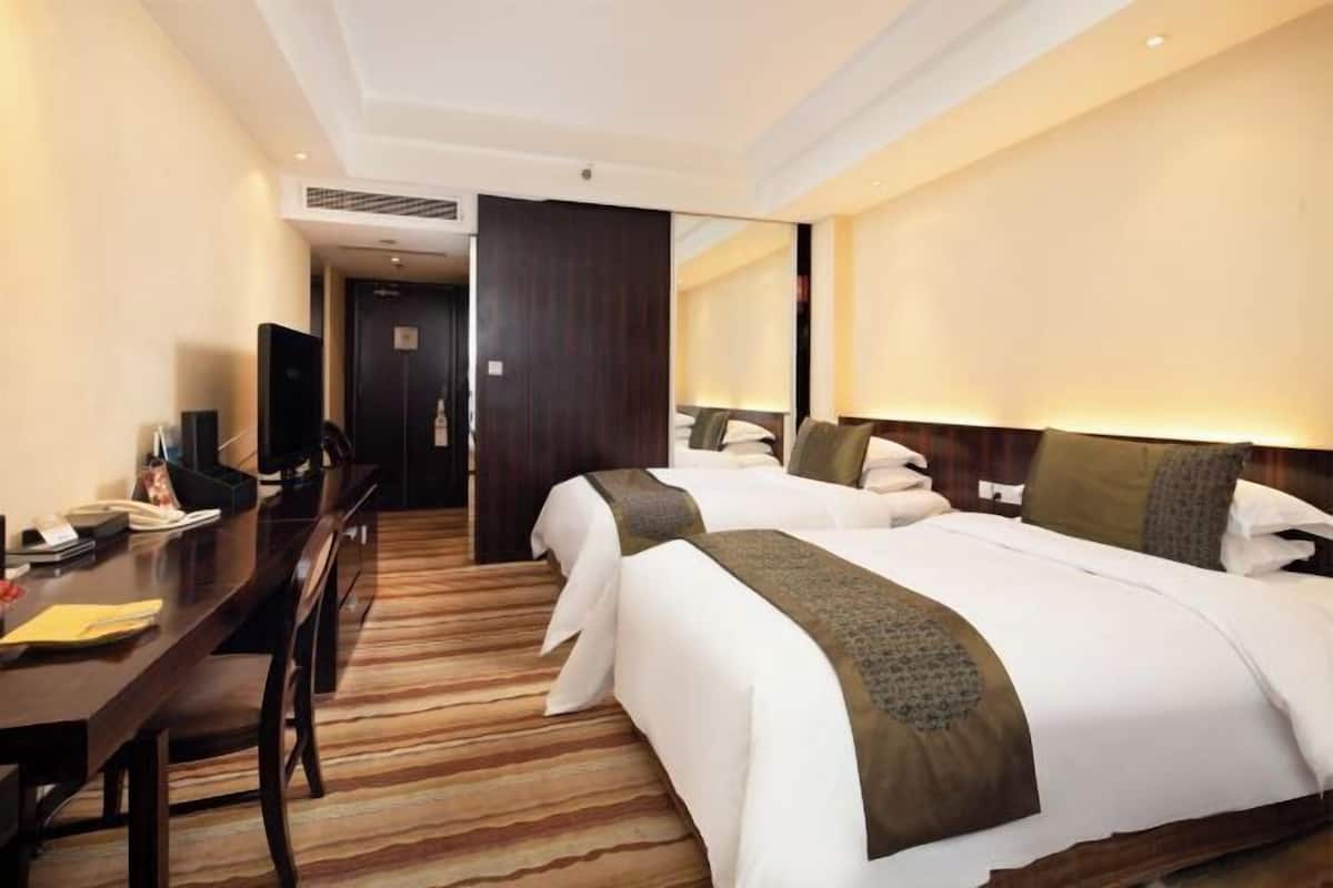 Habitación de hotel con dos camas, un escritorio, una silla y un televisor.
