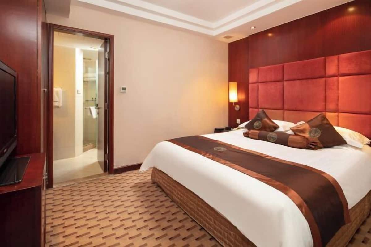 Habitación de hotel con una cama grande, cabecera de madera, televisión y baño visible a través de una puerta abierta.