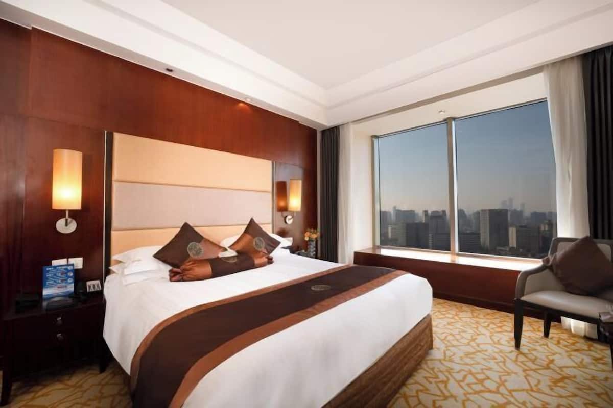 Habitación de hotel con una cama grande, vista a la ciudad, una mesita de noche y una silla.