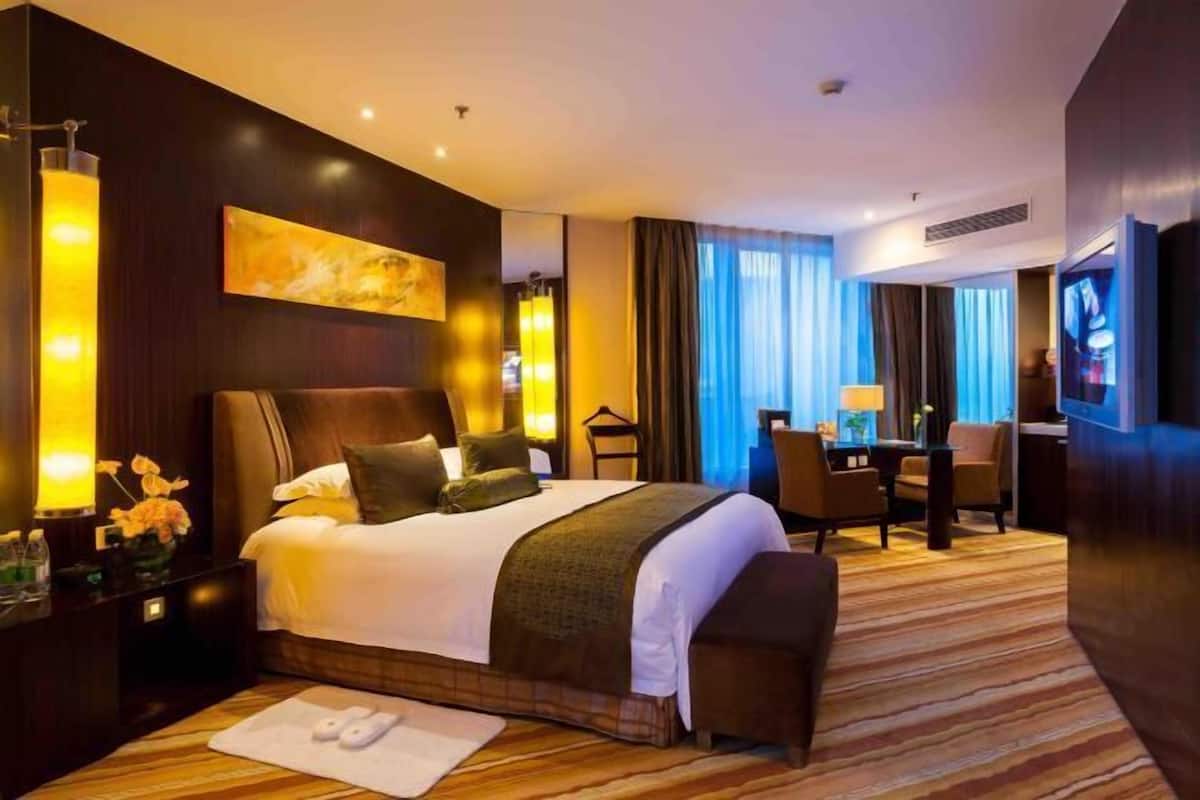 Habitación de hotel con una cama grande, un escritorio, una silla, un televisor y un cuadro en la pared.