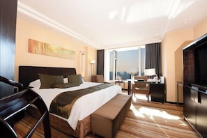 Ein Hotelzimmer mit einem großen Bett, einem Schreibtisch, einem Fernseher und Blick auf die Stadt.