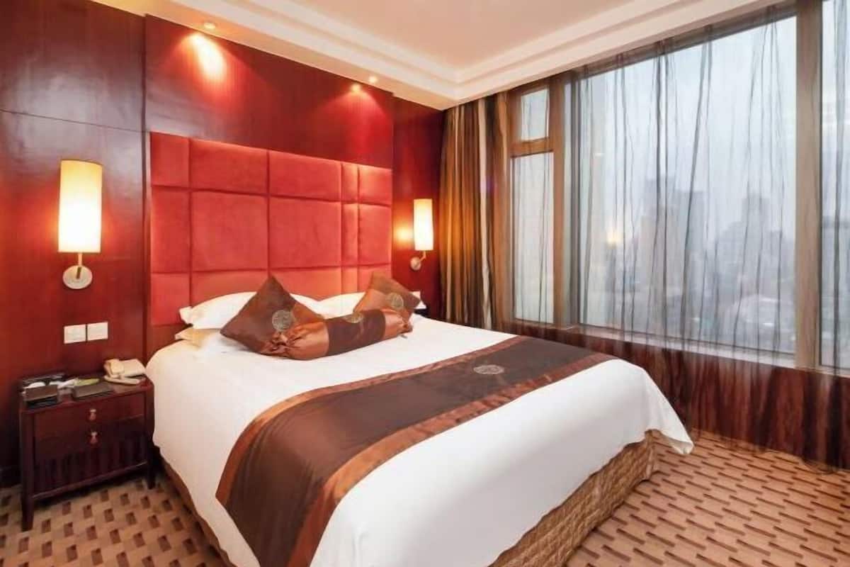 Habitación de hotel con una cama grande, un cabecero de madera, dos lámparas de noche, una mesita de noche y un ventanal con cortinas.