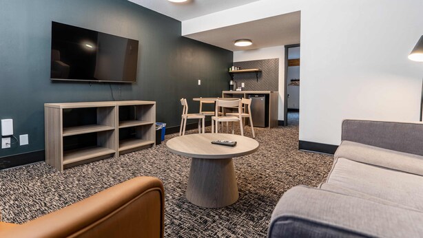 A modern living room with a flat-screen TV, a wooden TV stand, a round coffee table, and a sofa. - Northwinds Hotel Revelstoke (Revelstoke)