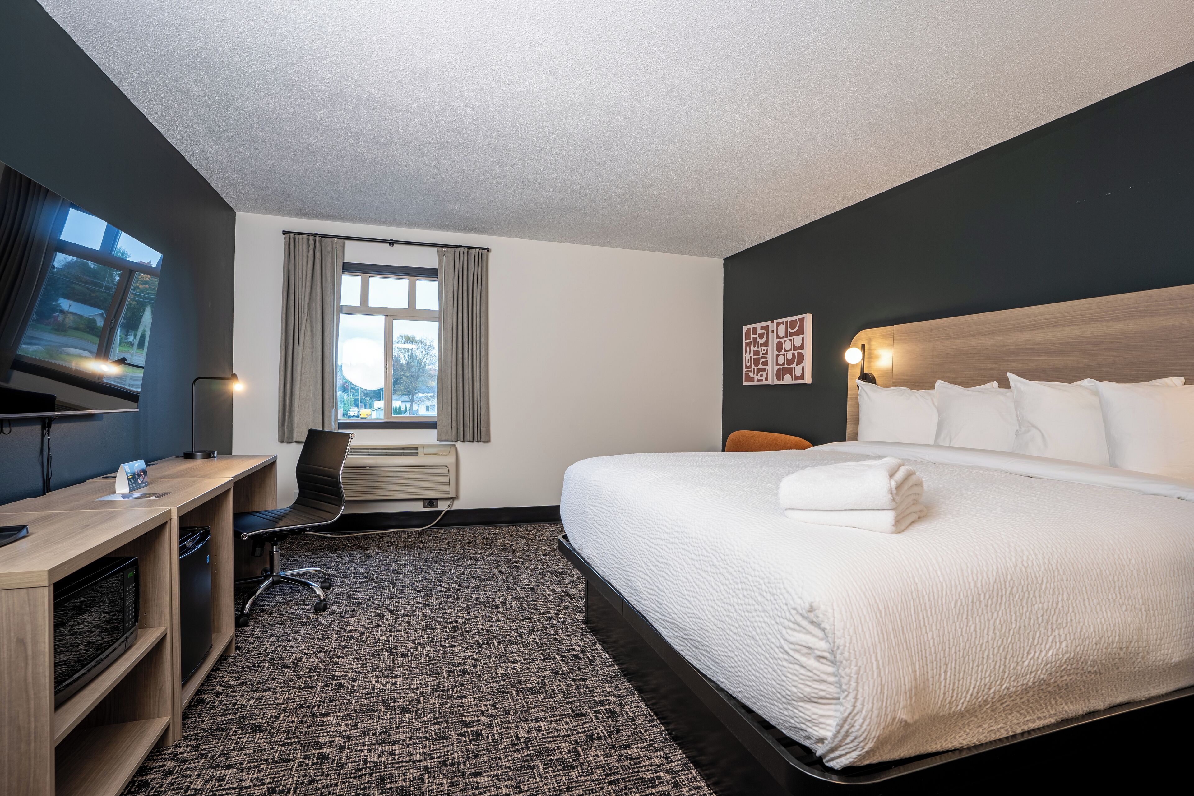 Een hotelkamer met een groot bed, een bureau met een computer, een stoel, een televisie en een raam met gordijnen.