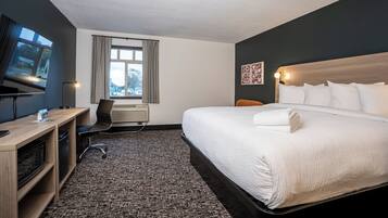 Een hotelkamer met een groot bed, een bureau met een computer, een stoel, een televisie en een raam met gordijnen.