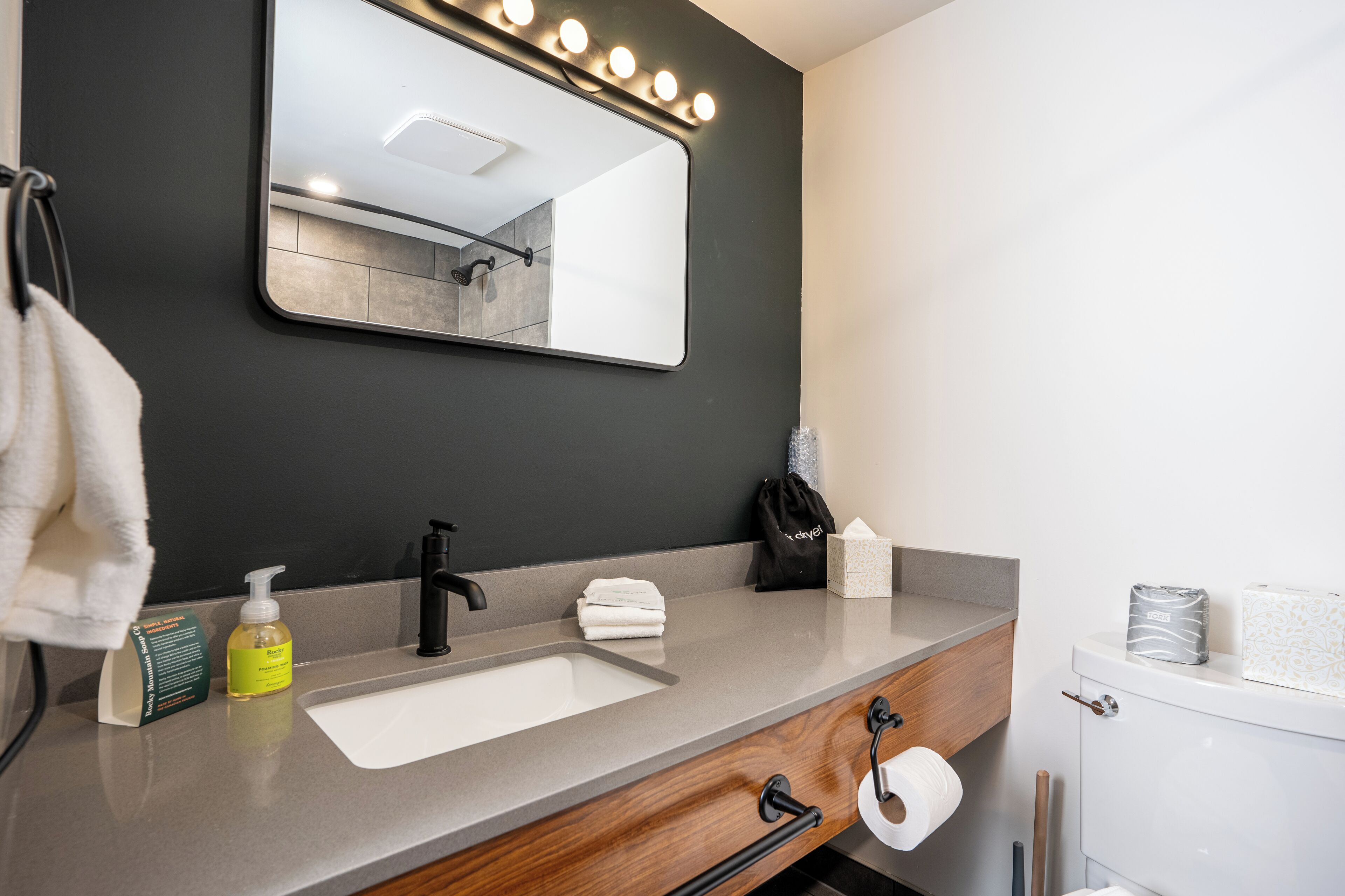 A modern bathroom with a large mirror, vanity, sink, and toilet.