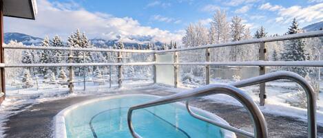 A pool area with a view of snow-covered trees and mountains.