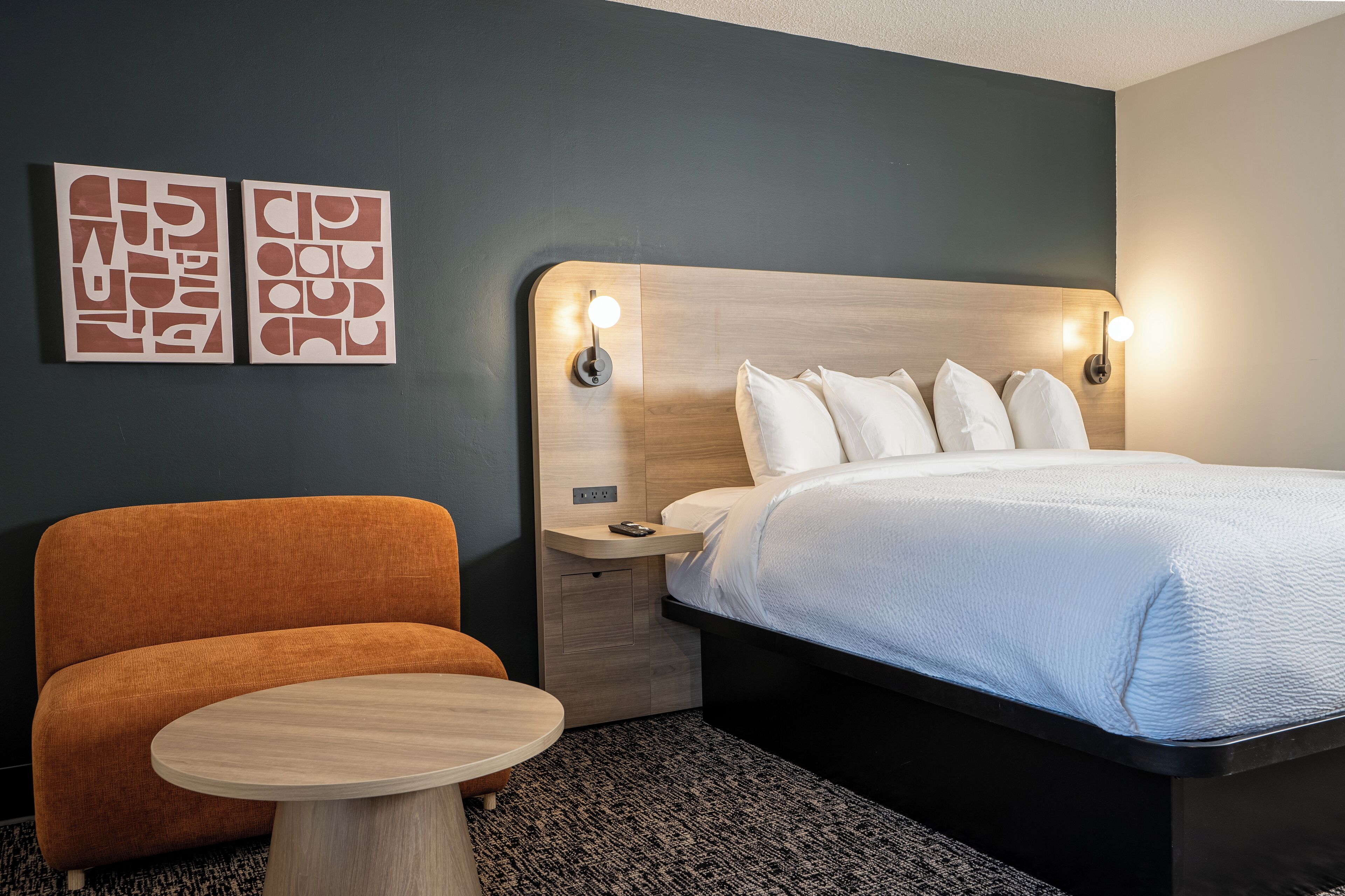 Une chambre d’hôtel comprenant un lit, une table de chevet, une chaise et deux œuvres d’art murales.