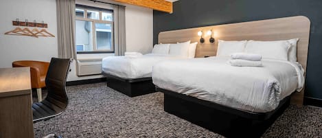 Habitación de hotel con dos camas, un escritorio, una silla y un ventanal con cortinas.