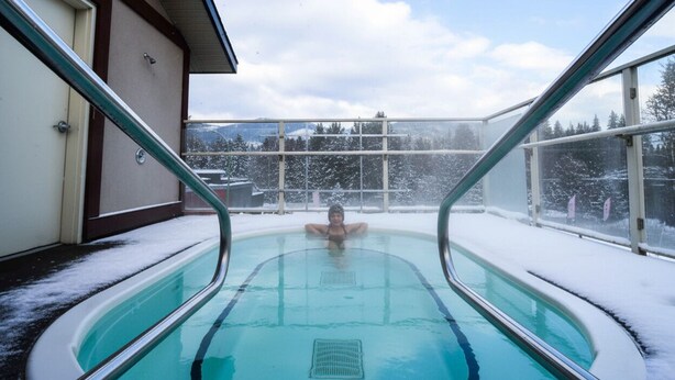 Una piscina interior con paredes de vidrio, rodeada de suelo y árboles cubiertos de nieve.