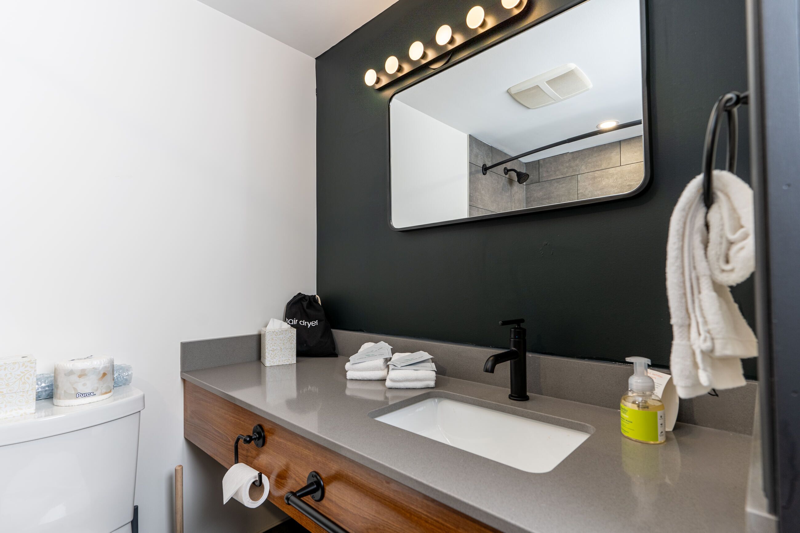 Een moderne badkamer met een wastafel, wasbak en spiegel. Er liggen handdoeken, een haardroger en toiletartikelen op het aanrecht.