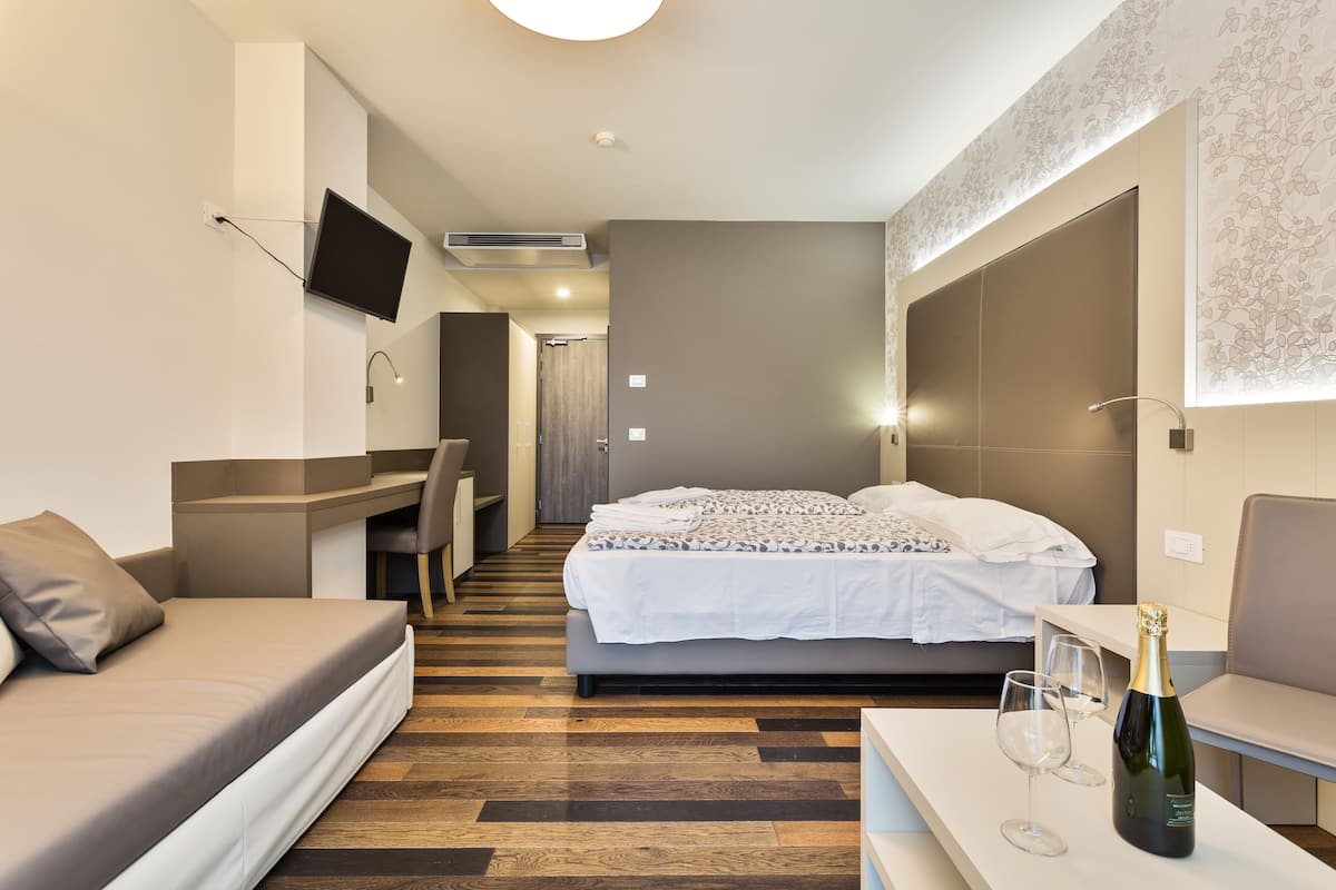 Una habitación de hotel moderna con una cama, un escritorio, una silla, un televisor montado en la pared y una botella de champán en la mesita de noche.