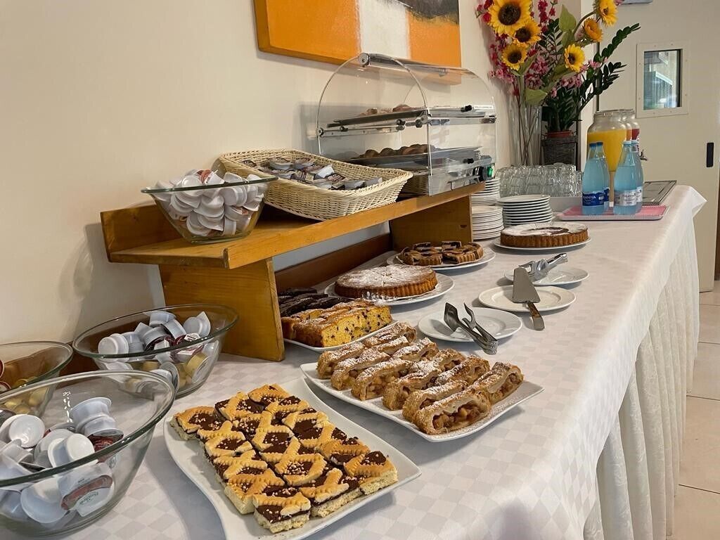 Una mesa de bufé con diversos pasteles y postres, un dispensador de jugo y un jarrón con girasoles.