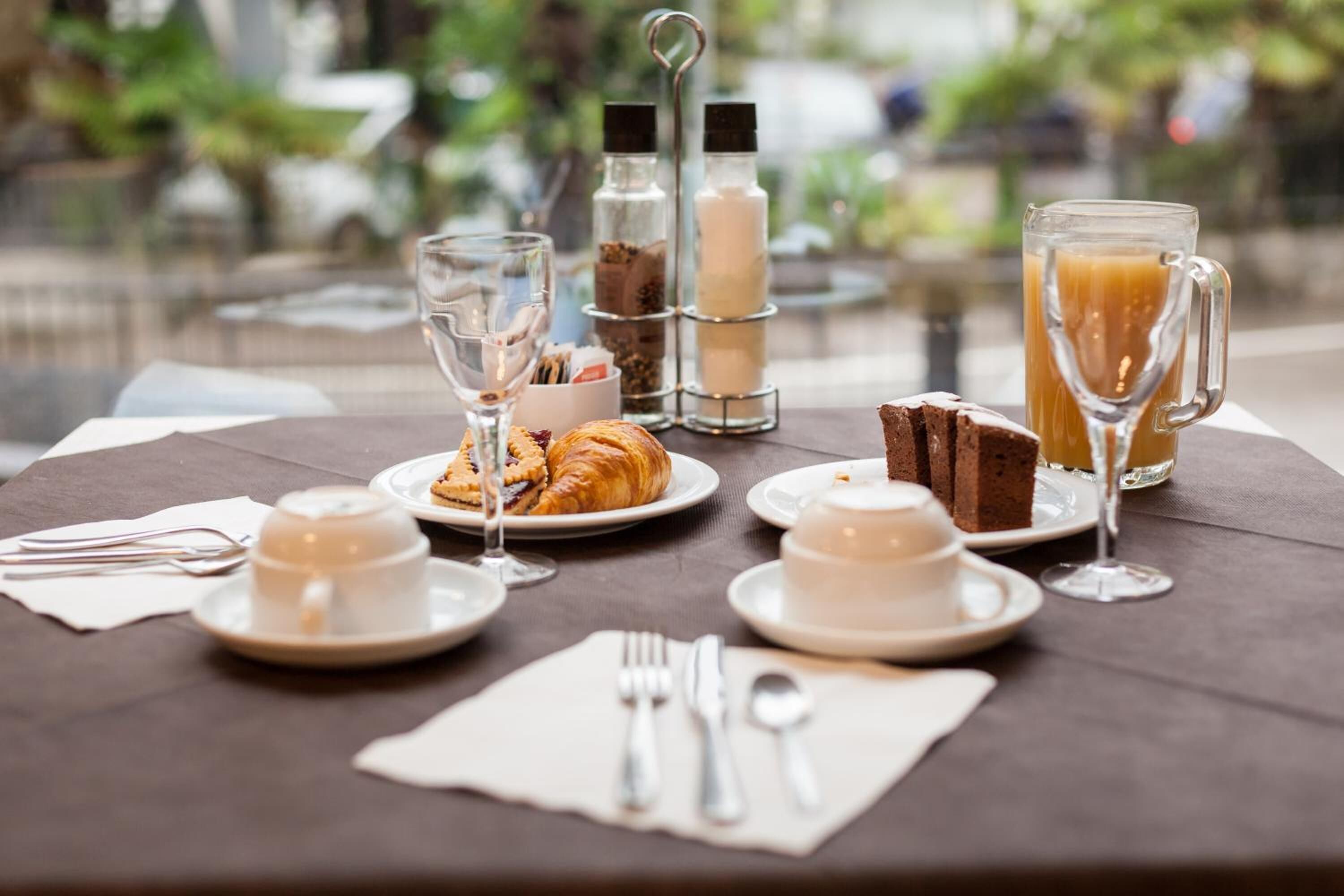 A breakfast table set with croissants, a cake, coffee cups, and a glass of orange juice.