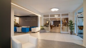 A modern hotel lobby with a reception desk, seating area, and a view into the dining area.