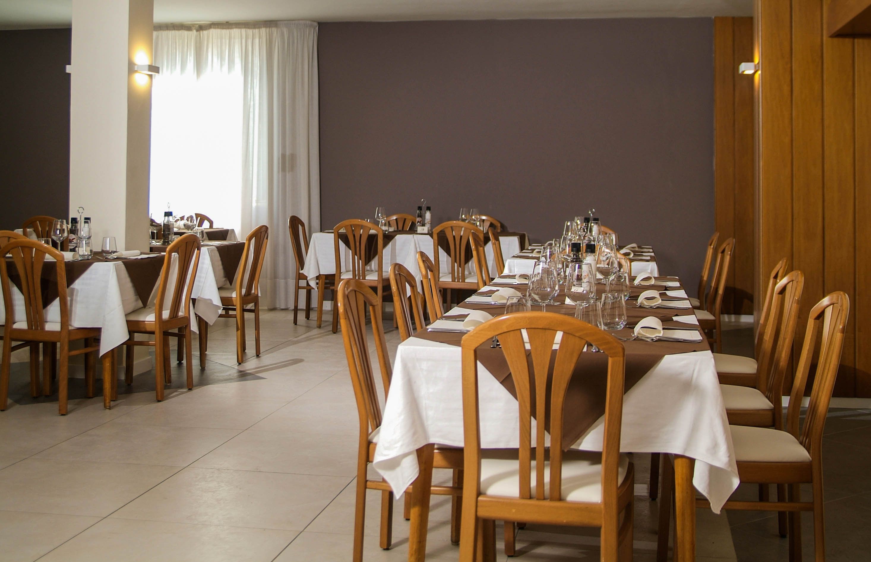 Un comedor con varias mesas dispuestas para el servicio, sillas de madera y una paleta de colores neutros.