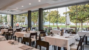 A restaurant with outdoor seating, large windows, and a view of the trees and sky.