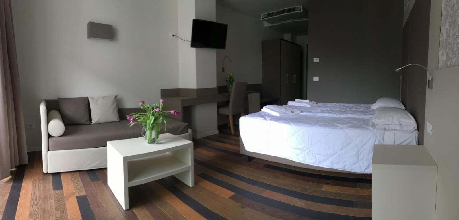 Hotelkamer met een bed, een bank, een kleine tafel met een vaas, een bureau en een televisie.