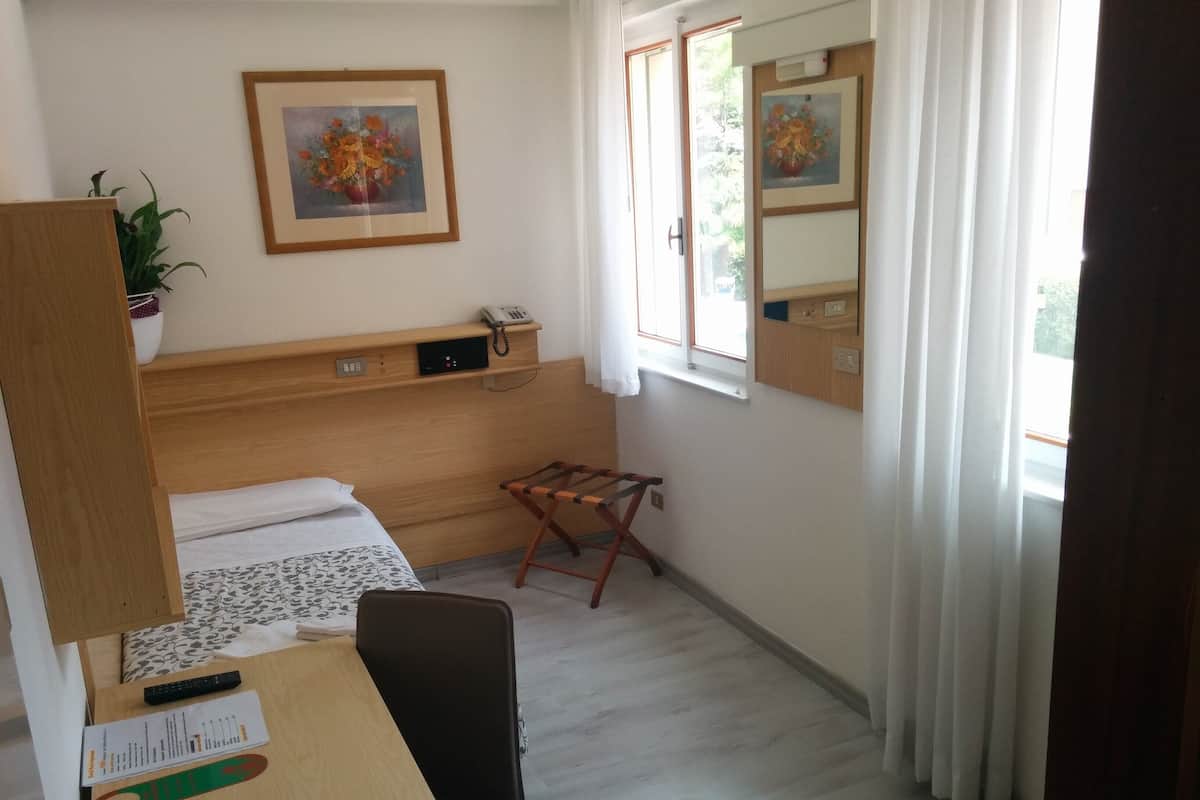 Habitación de hotel con cama, escritorio con silla, teléfono, planta y dos cuadros enmarcados con motivos florales.