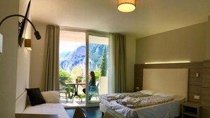 A hotel room with a bed, a desk, and a view of mountains through a large sliding door.