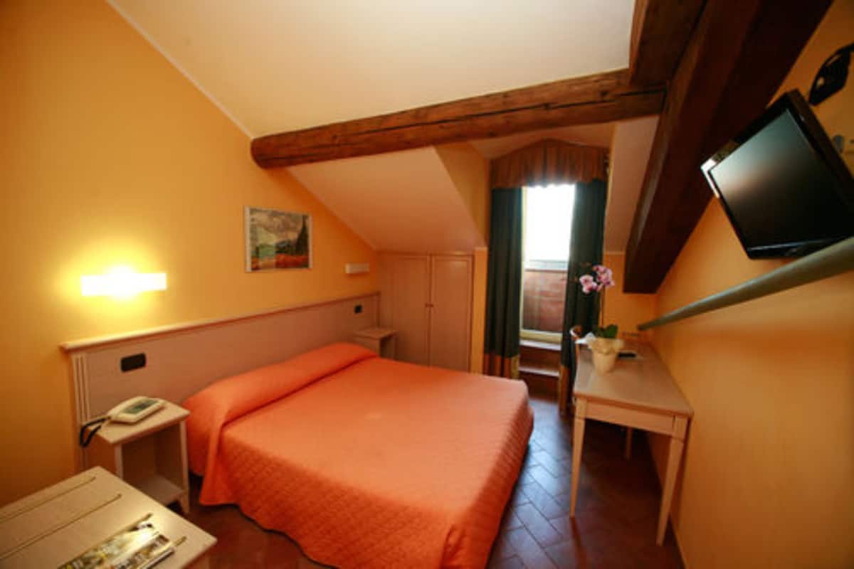 A room with a bed, a desk, a television mounted on the wall, and a window with curtains.