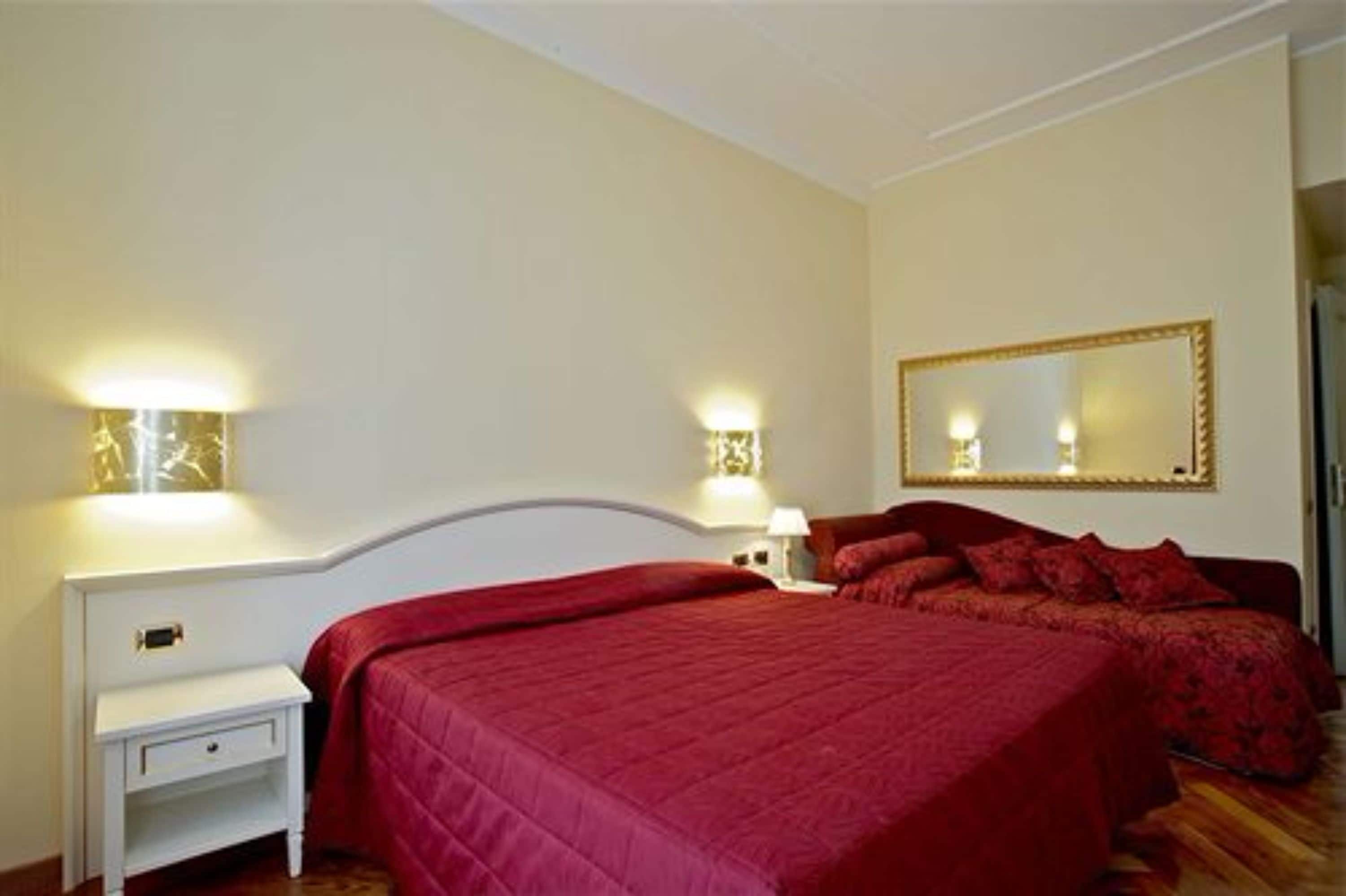 A bedroom with a large bed, two bedside tables, a nightstand, and a mirror on the wall.