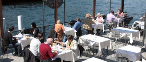 An outdoor dining area with tables and chairs, overlooking a body of water.