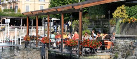 A riverside restaurant with outdoor seating, stone walls, and a view of the water.