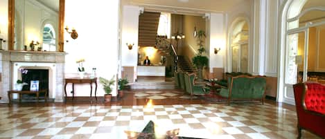 A lobby with a checkered floor, a star-shaped design, a fireplace, and a staircase leading to another level.