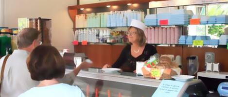 Mostrador de panadería con una vitrina de productos horneados y una cajera.