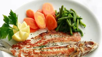 Ein Teller mit gegrilltem Fisch, Karottenstiften, grünen Bohnen, Zitronenspalten und Petersilie.