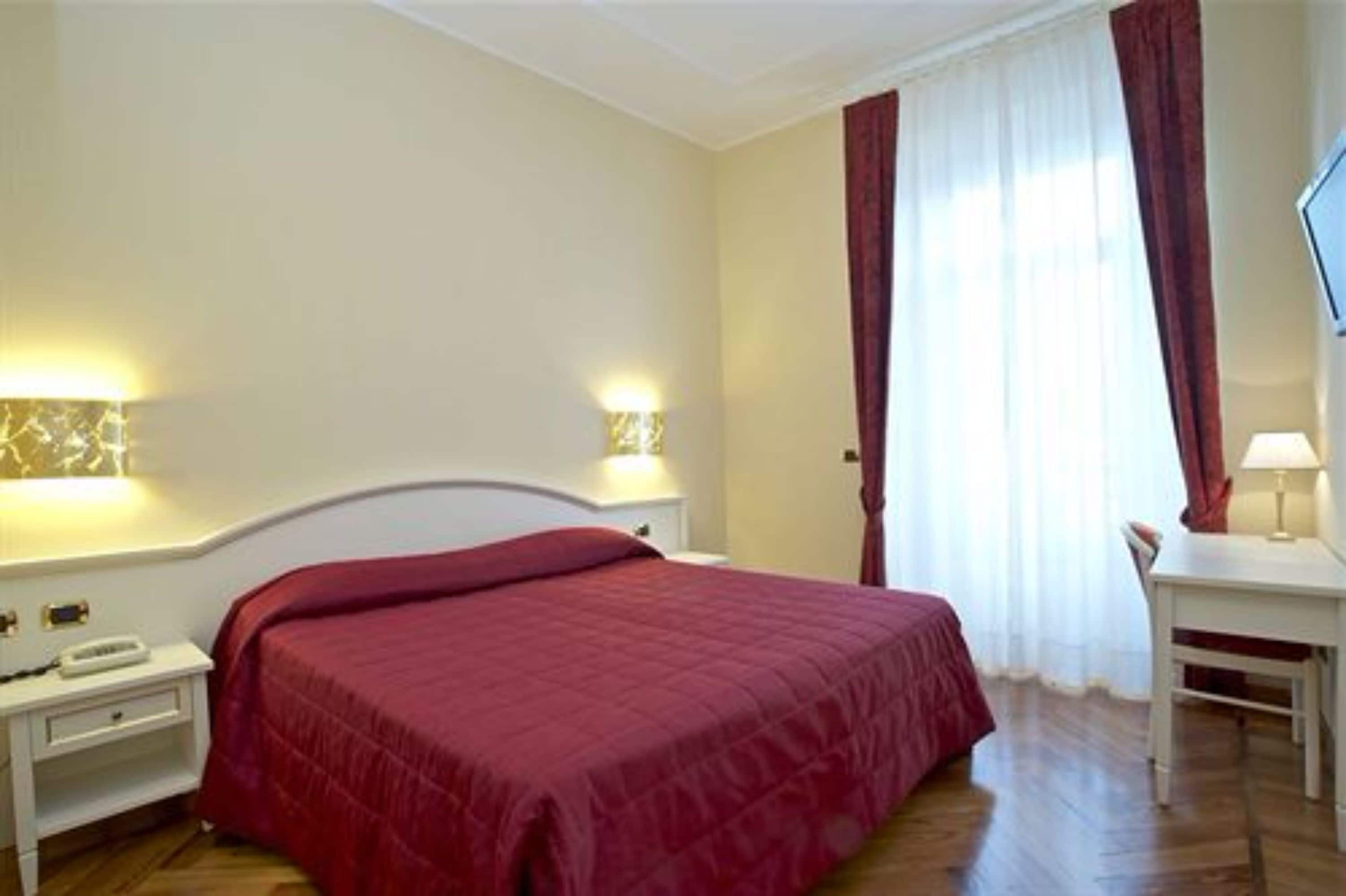 A hotel room with a bed, bedside tables, a desk, and a chair.