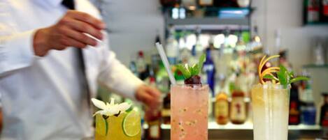Tres cócteles sobre la barra, con un barman al fondo.