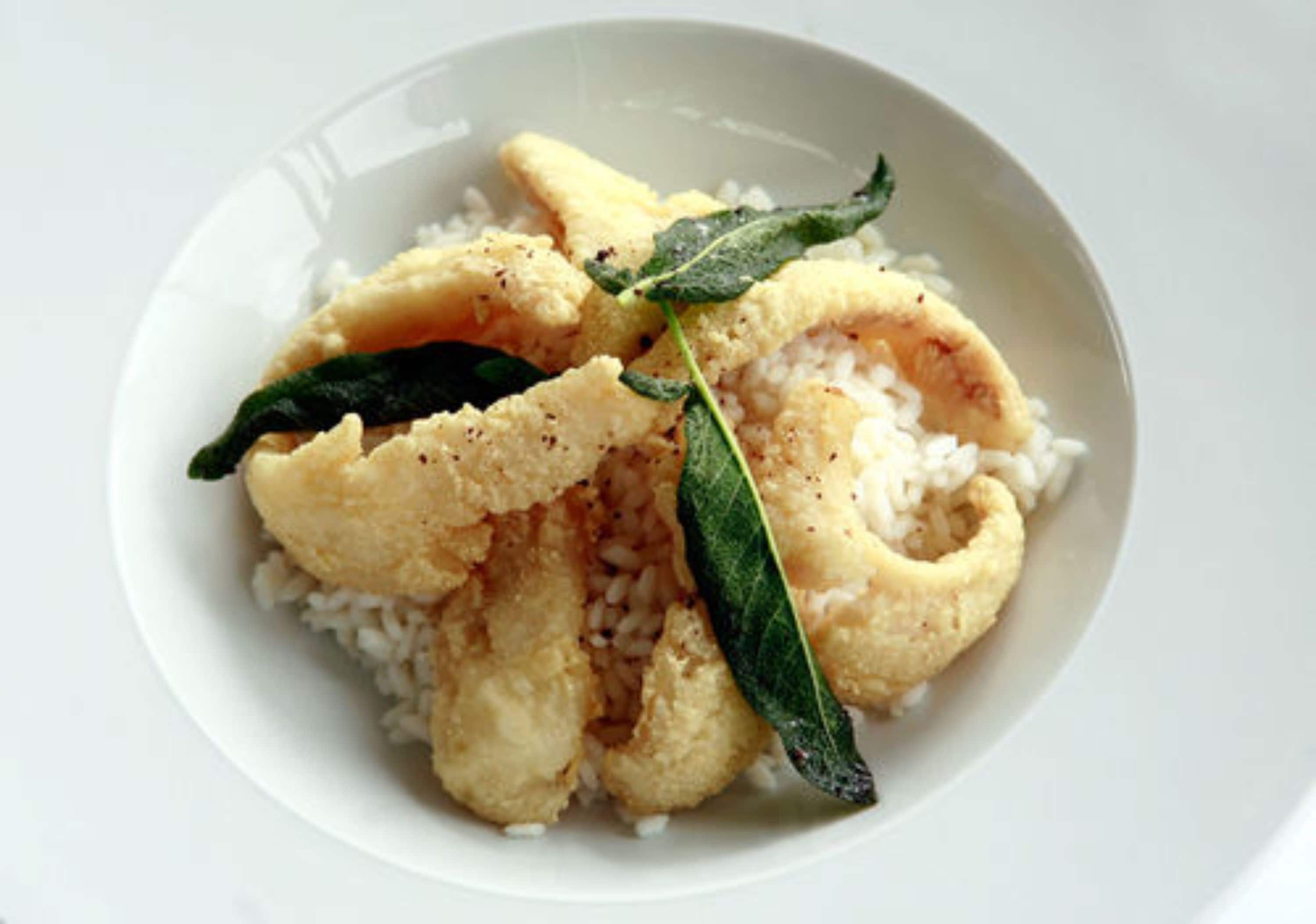 A plate with rice and fried items, possibly calamari, garnished with a leaf.
