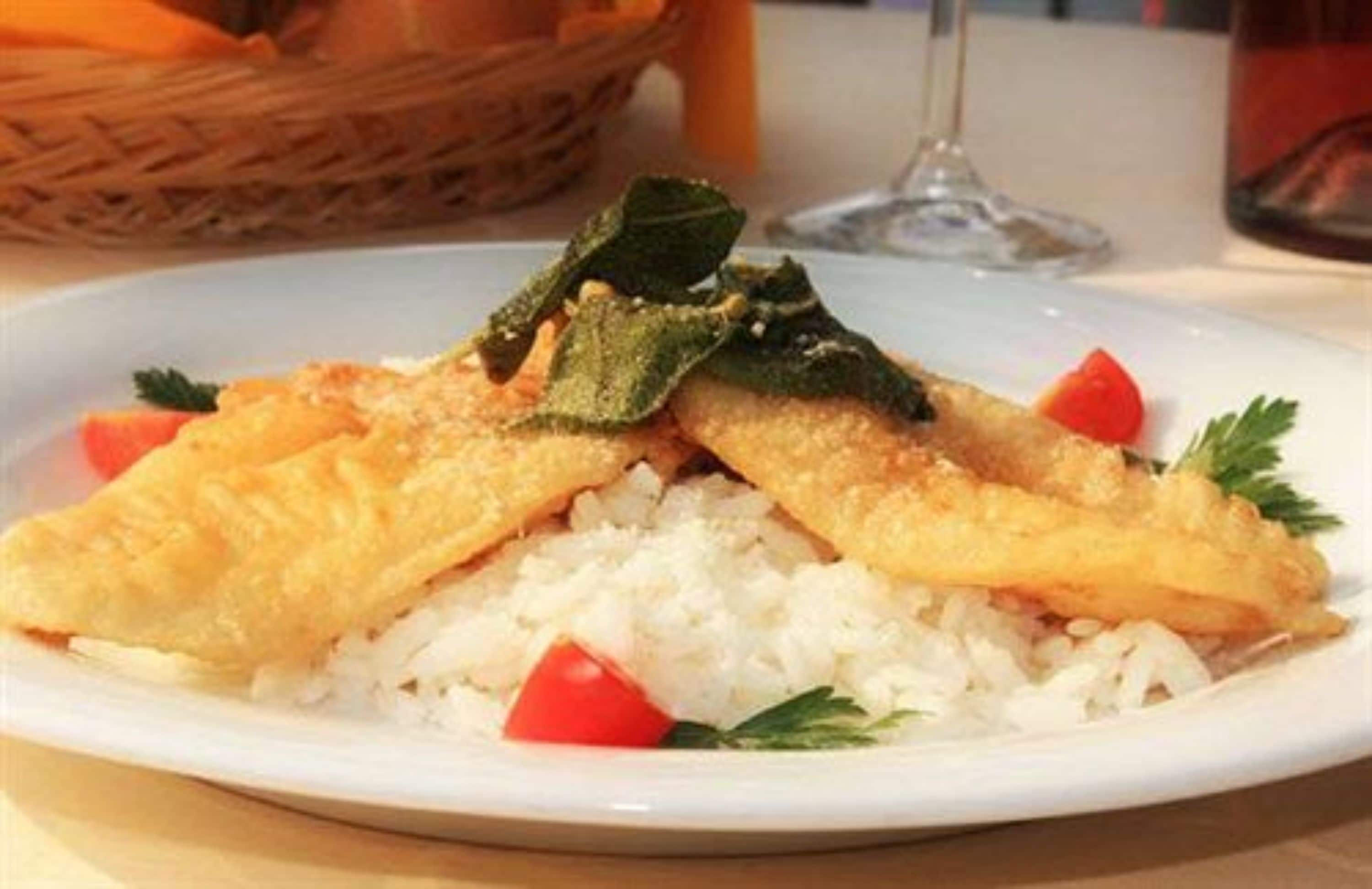 Un plato de pescado frito sobre arroz, con adorno de perejil y un tomate cherry.