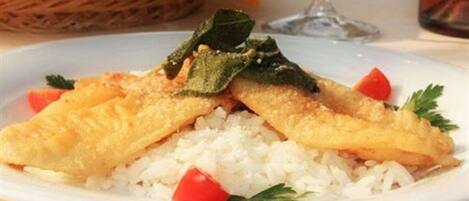 Un plato de pescado frito sobre arroz, con adorno de perejil y un tomate cherry.
