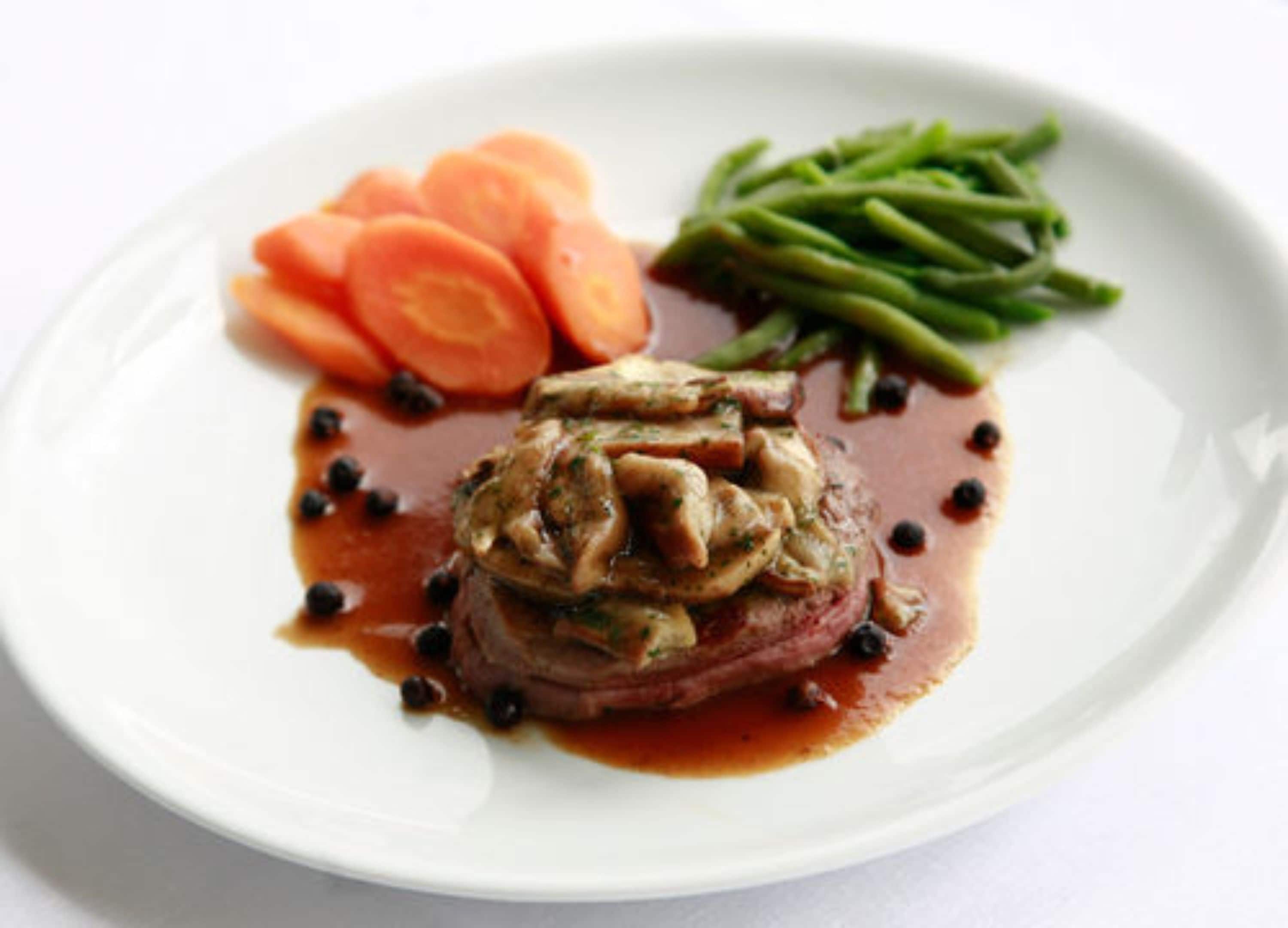 A plate with a steak topped with mushrooms and sauce, accompanied by sliced carrots and green beans.