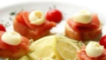 Un plato con alimentos, incluyendo salmón, tomates cherry y una cuña de limón.