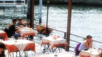 An outdoor dining area with tables and chairs, overlooking a body of water.