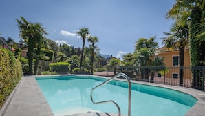 A rectangular swimming pool with a metal handrail, surrounded by a tiled deck and palm trees. - Hotel Excelsior Splendide (Bellagio)